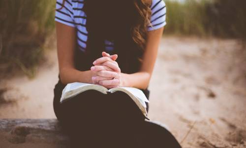 picture of a youth praying with her hands on a bible